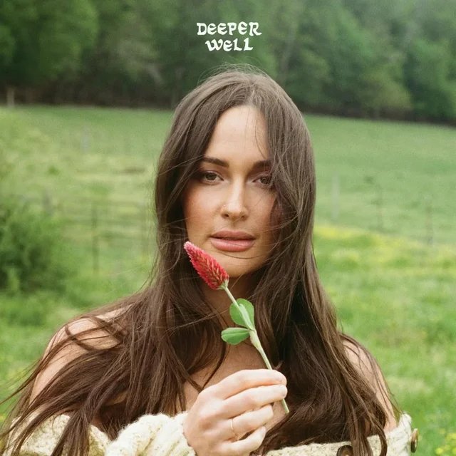 A woman with long brown hair holding a pink flower in a grassy field with trees in the background, and the words 'Deeper Well' above her head.