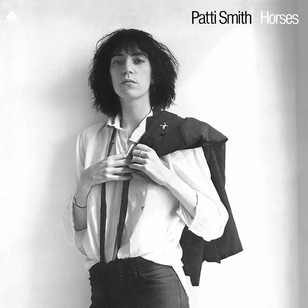 Black and white photo of Patti Smith holding a coat over her shoulder, wearing a white shirt and dark pants, on the album cover titled 'Horses'.